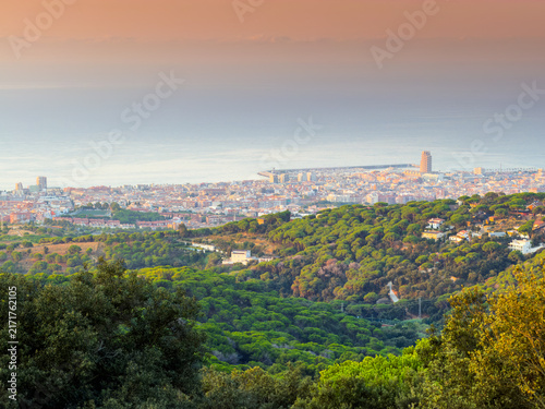 Scenic panoramic aerial view over coastal town of Mataro in Catalonia with green forested hills and calm Mediterranean Sea under warm sunset golden light.