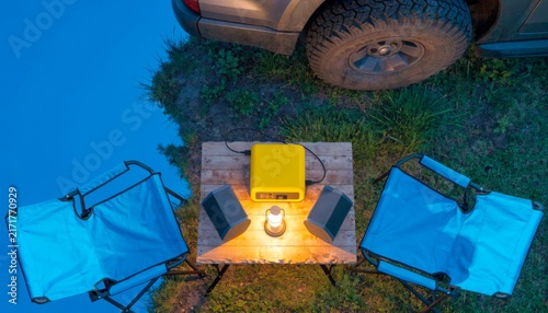 Camping setup with chairs, table, and lantern near vehicle at dusk