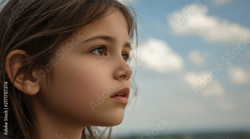 Close up face little girl looking into distance beneath cloudy sky