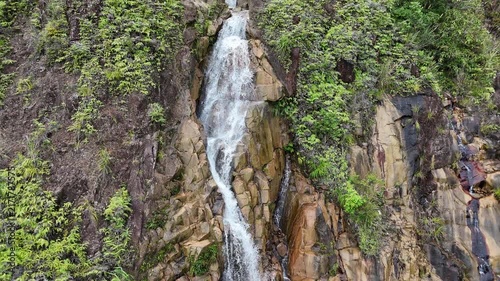 Aerial Drone Pullback from a Small Waterfall Along Khanh Le Pass in Lam Dong, Vietnam, Gradually Revealing the Full Height of the Tall Cascade Surrounded by Lush Mountain Forest