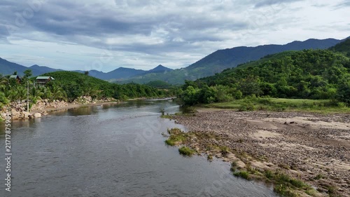 Aerial Drone Flight Over a Crystal Clear Peaceful Stream Flowing Beside a Beautiful Rocky Gravel Bank, Showcasing Fresh Water, Natural Stones, and Serene Tropical Scenery