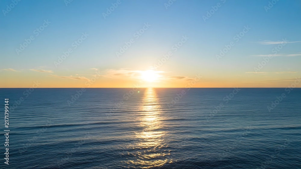 Fototapeta premium Golden sunrise over the calm ocean horizon with soft blue sky and gentle ripples on the water surface during a peaceful early morning landscape view