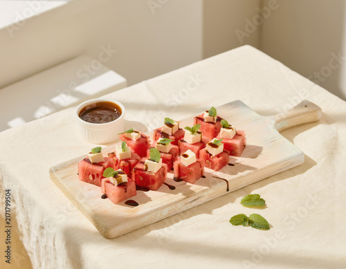 Delicious refreshing watermelon and feta cheese bites with fresh mint leaves and balsamic glaze beautifully arranged on a rustic wooden board for a healthy summer appetizer