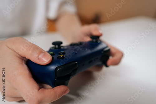 Obraz na plátně Close-up of female gamer hands adjusting modern navy blue wireless video game controller, preparing for online multiplayer gaming, leisure activity, digital fun on sitting at white table