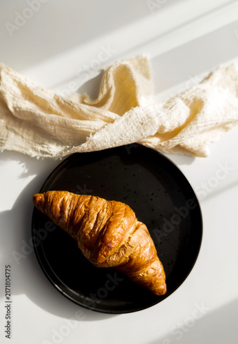  Fresh French croissant on a black plate and coffee in a reusable travel mug
