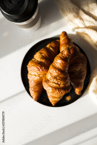 Fresh French croissant on a black plate and coffee in a reusable travel mug