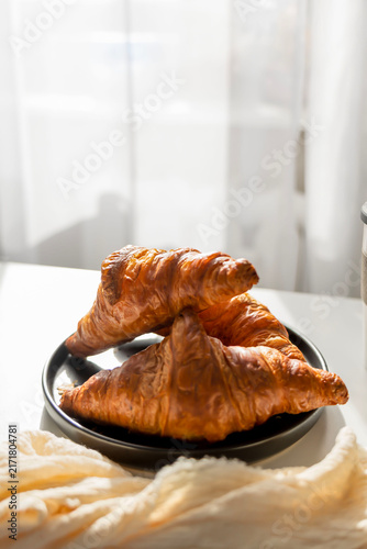  Fresh French croissant on a black plate and coffee in a reusable travel mug