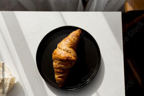  Fresh French croissant on a black plate and coffee in a reusable travel mug