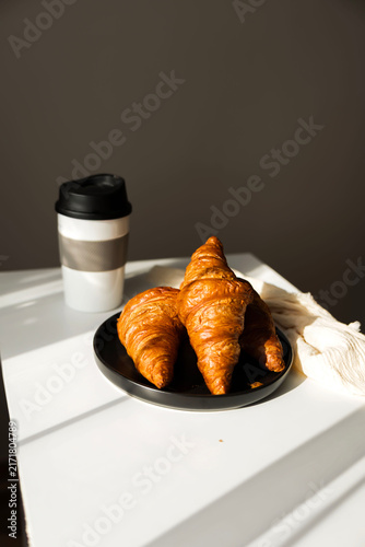  Fresh French croissant on a black plate and coffee in a reusable travel mug