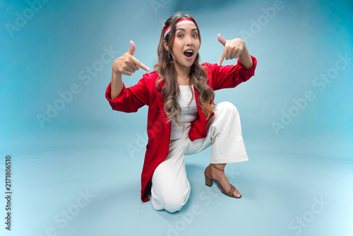 Cute young Indonesian woman is sitting on the floor and pointing to the copy space below.