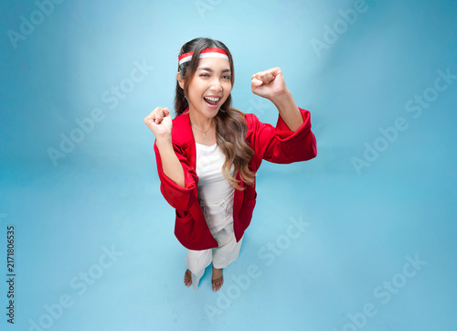 Joyful young Asian woman is raising fists doing celebration gesture.