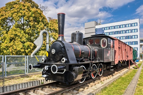 Картината върху платно Historic black steam locomotive engine with red wheels and wooden cargo wagon displayed outdoors on tracks under a blue sky