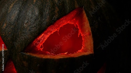 Spooky 4K Seamless Loop Close-up of Carved Jack-o'-Lantern Eye with Eerie Red Glowing Light and Dark Texture Background