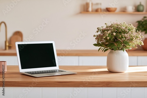 Laptop mock up on a kitchen counter with a wooden surface, a vase of flowers, and a pink mug, creating a minimalistic and modern workspace setting