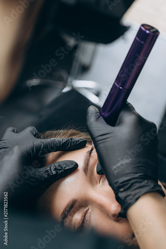 Permanent makeup artist performs an eyebrow tattoo procedure after mapping the shape, creating natural brows with a PMU machine in a professional beauty studio.