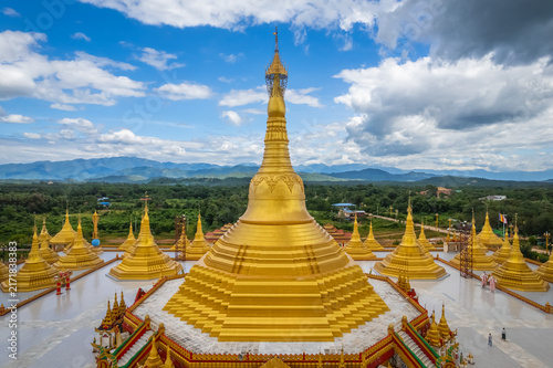 Obraz na plátne Aerial view of a golden stupa surrounded by smaller pagodas with lush green hill