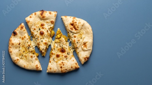 Garlic naan bread is sliced into four pieces on a blue background.