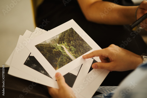 Quadro su tela Hands of young Asian man holding and pointing at printed landscape photos during