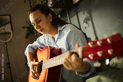 Photography Caucasian young woman playing acoustic guitar at home, practicing chords
