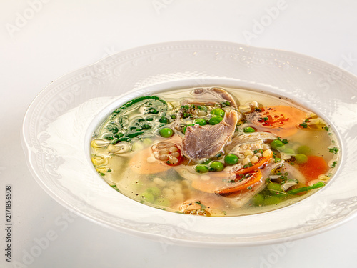 Foto Chicken soup with carrots peas and herbs in white bowl