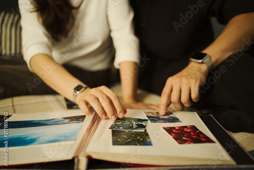 Cropped shot of young couple looking at printed photos in album, reminiscing about travel memories. Ideal for family lifestyle and photography services marketing
