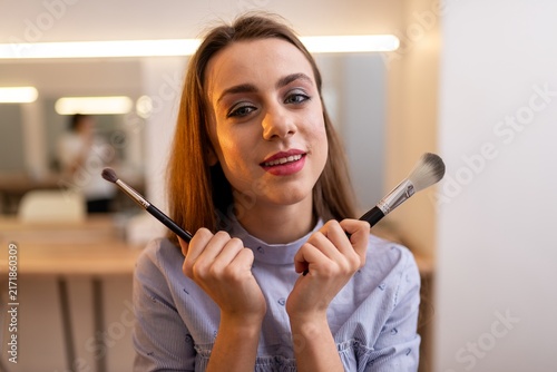 Foto Young smiling woman holding cosmetic brushes in a beauty studio