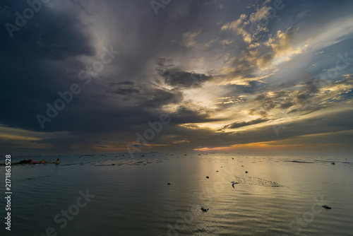 Stormy Sunset Over Ocean: Dramatic clouds gather as the sun dips below the horizon, casting a warm, golden light across the calm ocean surface, dotted with distant boats.