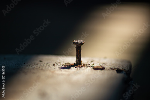 Obraz na plátně Macro of an old rusty iron nail driven into weathered wood plank illuminated by a dramatic beam of light