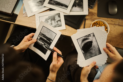 фотографія Hands of unrecognizable editors holding black and printed photos at desk, reviewing portfolio