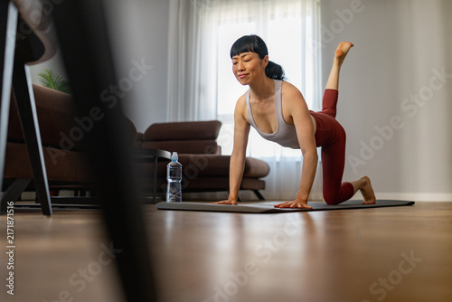 Canvastavla Woman practicing yoga at home doing a leg raise plank on a mat in living room