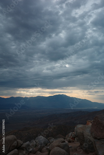 Dramatic storm clouds with sun rays over a desert mountain valley overlook in Joshua Tree National Park, California