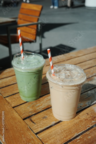 Two iced drinks in plastic cups on a wooden outdoor table with blurred pedestrian legs, Los Angeles, California
