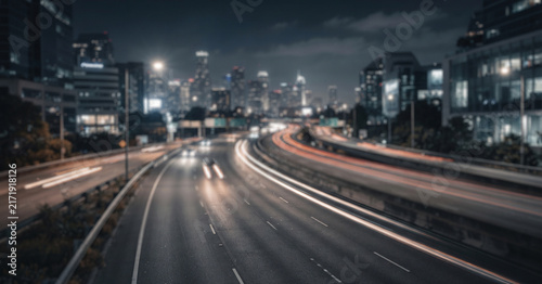 A fully blurred highway through a modern city, with soft vehicle lights, distant buildings, atmospheric haze, and flowing motion, designed as a minimal cinematic road background.