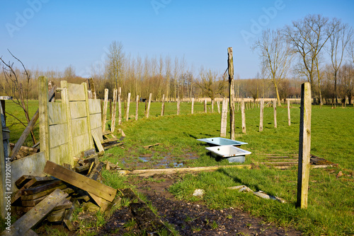 Quadro su tela An agricultural pasture featuring old wooden fences, discarded timber debris, and two bathtubs repurposed as animal water troughs under a clear blue sky surrounded by bare trees