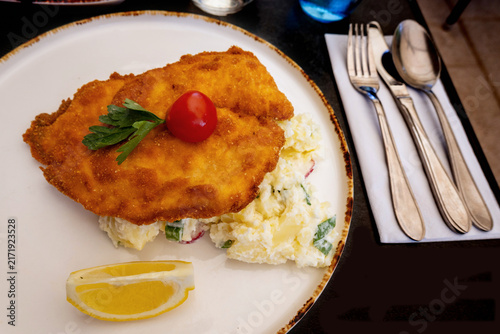 Konstfotografi Pork schnitzel with potato salad, lemon on plate, cutlery.