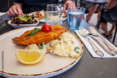 Konstfotografi Pork schnitzel with potato salad and lemon on plate, cutlery, beverage, man
