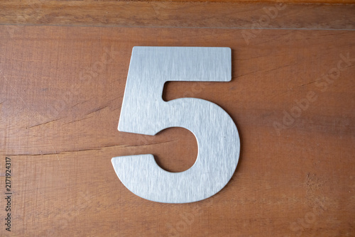 Brushed metal house number five mounted on a wooden texture background