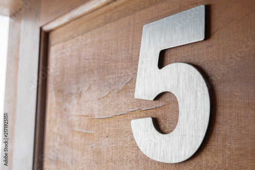 Brushed metal house number five mounted on a wooden texture background