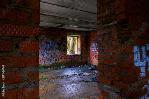 Фотография Dim derelict brick interior with rough mortar walls, graffiti, debris strewn con
