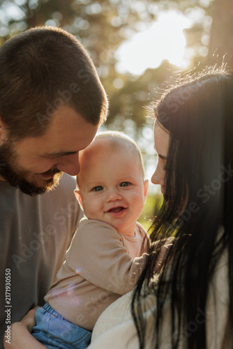 Happy baby smiling between parents in warm sunlight outdoors