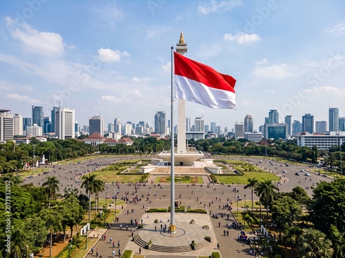Red and White Flag Waving Above a Crowded City Monument During a Celebration