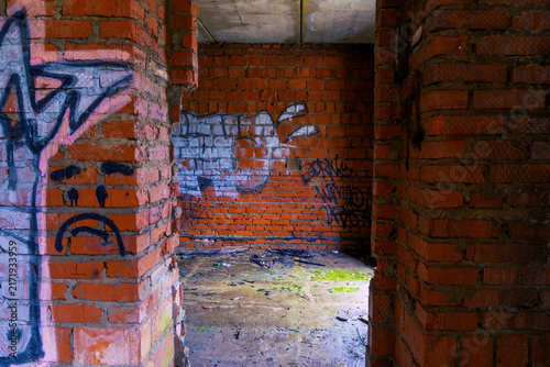 Photography View through rough brick doorway into abandoned interior with colorful graffiti,