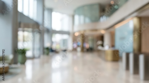 Blurred lobby of a corporate office building featuring a spacious reception area with marble floors and glass walls. Bright natural light fills the open architectural space.