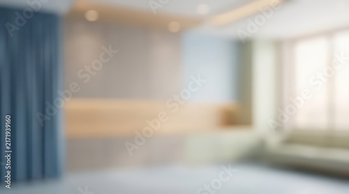 Blurred interior view of a contemporary living space with soft ambient lighting. The room features a minimalist wall design with wooden accents and blue curtains near a window.