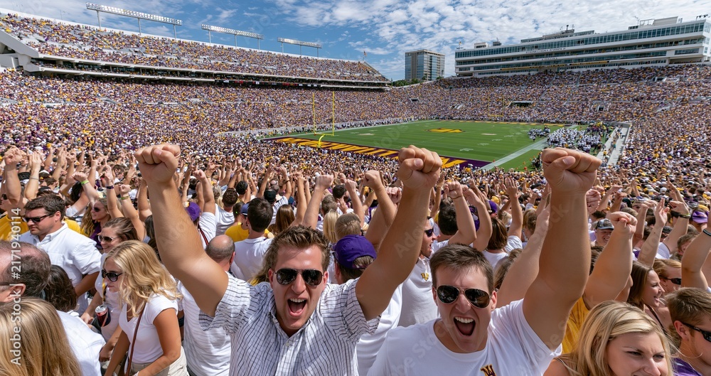 Naklejka premium Cheering crowd fills a colorful college football stadium, radiating energy and school pride on game day.