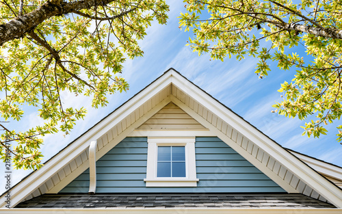 Residential house gable roof with white gutters and siding under blue sky