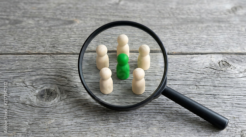 Magnifying Glass Focusing on a Unique Green Wooden Figure Among Plain Neutral Figures
