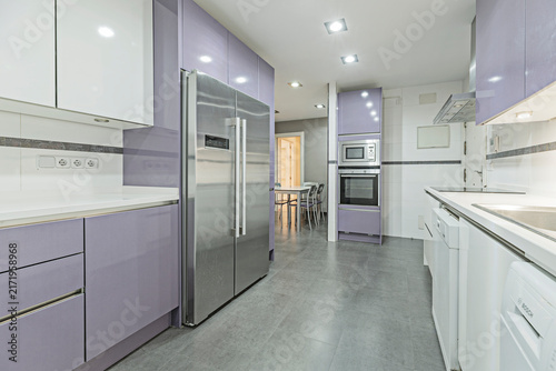 Bild auf Leinwand Galley kitchen with lavender cabinetry, built-in oven and microwave, stainless fridge, and a dining area visible beyond