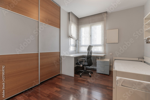 Bedroom with two-tone wardrobe, corner desk and office chair, small dresser, and daybed near a curtained window.