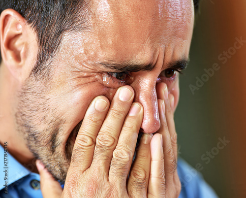 Close up of a distressed middle aged man crying with tears streaming down his face.